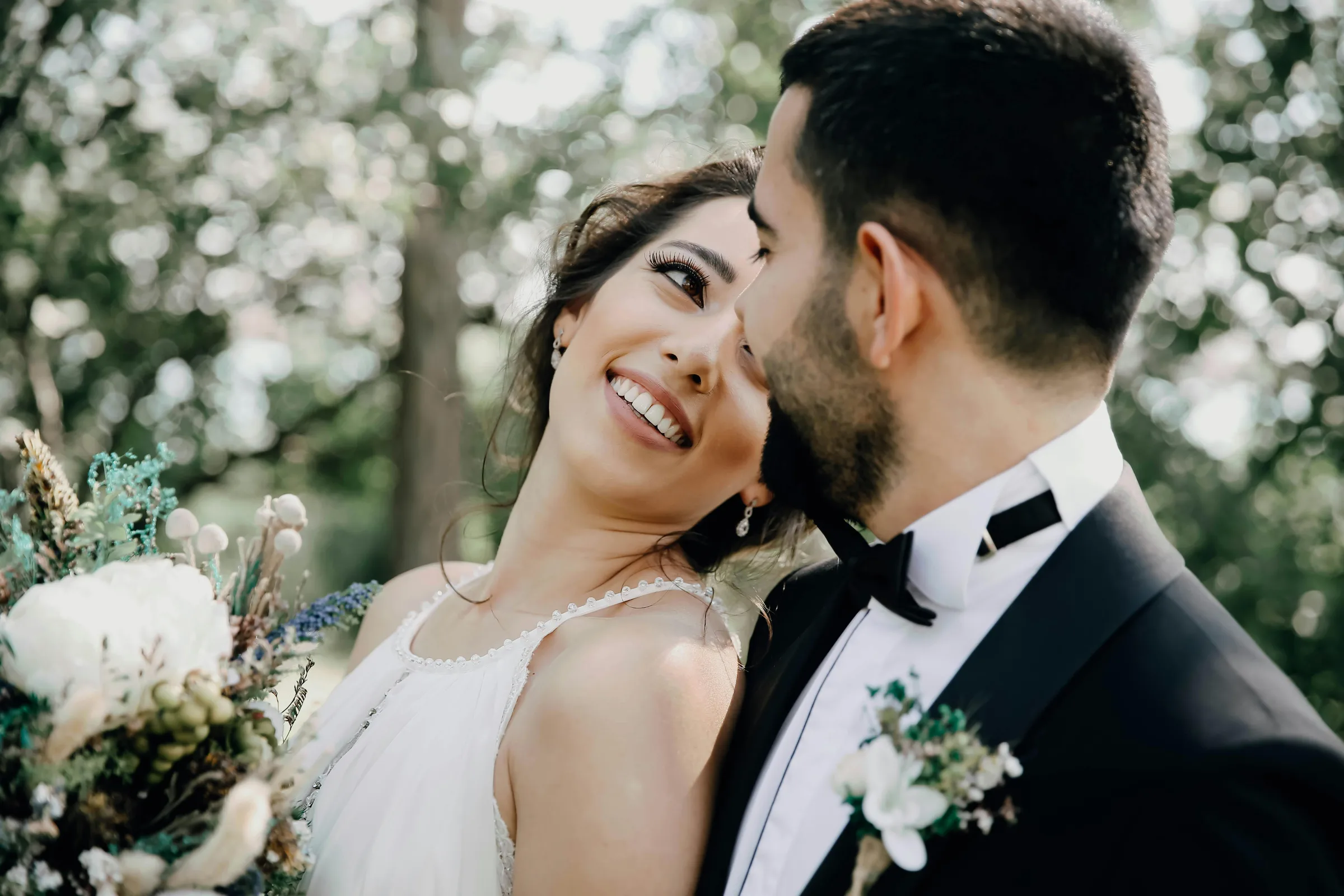 Braut lehnt lächelnd an ihrem Bräutigam, beide im Wald bei ihrer Hochzeit